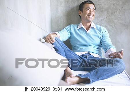 Mid adult man sitting on a bed operating a mobile phone View Large Photo Image Stock Image - Mid adult man sitting on a bed operating a mobile phone. Fotosearch