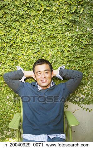 Mid adult man sitting on a chair with his hands behind his head View Large Photo Image Stock Image - Mid adult man sitting on a chair with his hands behind his head. Fotosearch