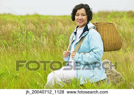 Mid adult woman sitting in tall grass holding a basket View Large Photo Image Stock Photo - Mid adult woman sitting in tall grass holding a basket. Fotosearch