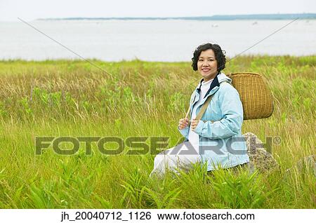 Mid adult woman sitting in tall grass holding a basket View Large Photo Image Stock Photograph - Mid adult woman sitting in tall grass holding a basket. Fotosearch