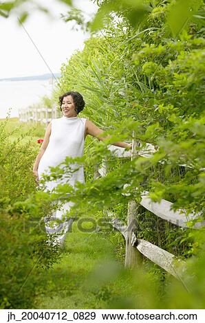 Mid adult woman standing leaning against a fence View Large Photo Image Stock Photo - Mid adult woman standing leaning against a fence. Fotosearch