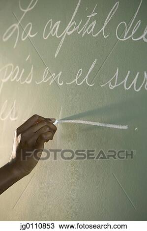 Stock Image - Person's hand writing with chalk on a chalk board. Fotosearch
