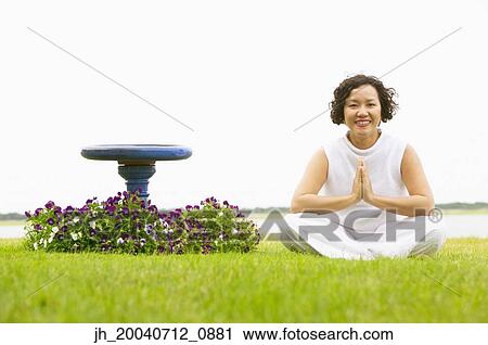 Stock Image - Portrait of a mid adult woman sitting meditating outdoors. Fotosearch