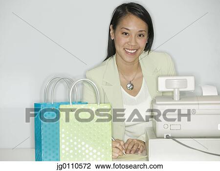Stock Image - Portrait of a woman standing at a cash register with shopping bags. Fotosearch