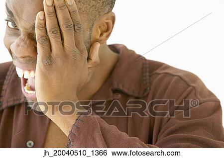 Stock Photograph - Portrait of a young man covering his eye with his hand. Fotosearch
