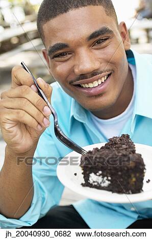 Portrait of a young man eating a piece of cake View Large Photo Image Stock Image - Portrait of a young man eating a piece of cake. Fotosearch