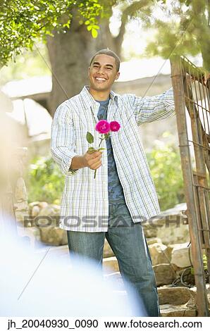 Portrait of a young man standing holding a rose View Large Photo Image Stock Image - Portrait of a young man standing holding a rose. Fotosearch