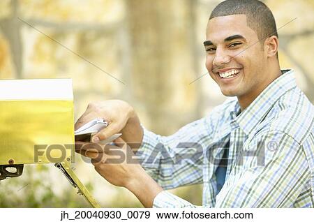 Portrait of a young man taking out mail from a mail box View Large Photo Image Stock Photo - Portrait of a young man taking out mail from a mail box. Fotosearch