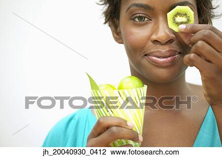Portrait of a young woman holding a slice of kiwi fruit over her eye View Large Photo Image Stock Image - Portrait of a young woman holding a slice of kiwi fruit over her eye. Fotosearch