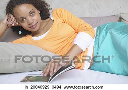 Picture - Portrait of a young woman lying down reading a book. Fotosearch