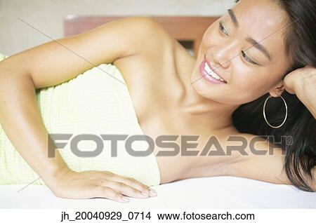 Portrait of a young woman lying on a bed with her hand on her head View Large Photo Image Picture - Portrait of a young woman lying on a bed with her hand on her head. Fotosearch