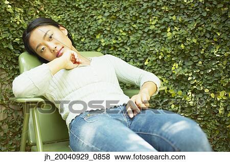 Portrait of a young woman sitting on a chair outdoors View Large Photo Image Stock Photo - Portrait of a young woman sitting on a chair outdoors. Fotosearch
