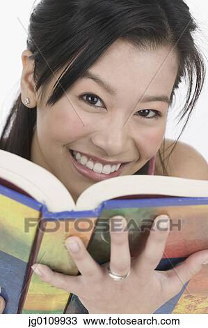 Stock Image - Teenage girl holding a book looking at camera smiling. Fotosearch