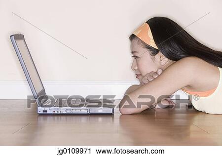 Stock Image - Teenage girl leaning forward on a table in front of a laptop. Fotosearch
