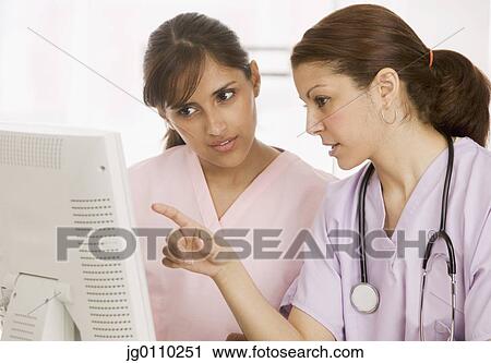Stock Image - Two nurses discussing in front of a computer monitor. Fotosearch