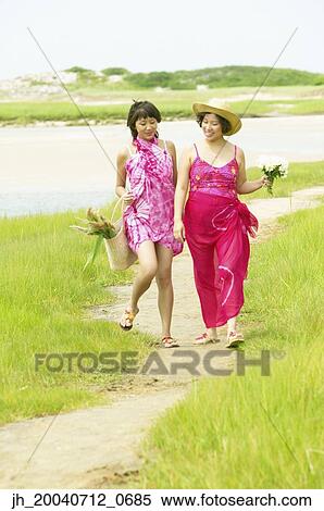 Two women walking on a path holding flowers View Large Photo Image Stock Photography - Two women walking on a path holding flowers. Fotosearch
