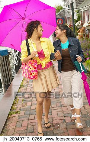 Two young women walking under an umbrella talking View Large Photo Image Stock Photography - Two young women walking under an umbrella talking. Fotosearch