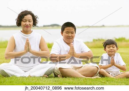 Stock Photograph - Woman and two young boys mediating on a lawn. Fotosearch
