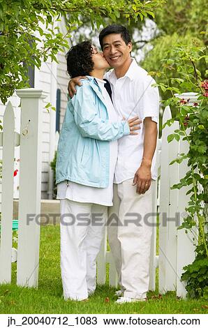 Woman kissing a man standing together on a lawn View Large Photo Image Stock Image - Woman kissing a man standing together on a lawn. Fotosearch