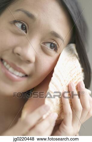 Stock Photo - Woman listening to a conch shell. Fotosearch