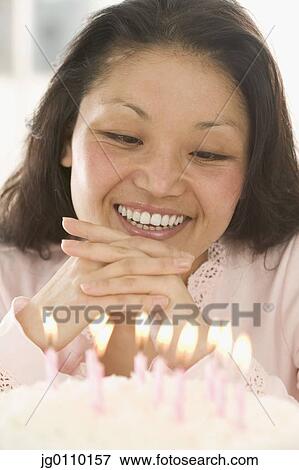 Stock Photo - Woman looking at lit candles on a cake smiling. Fotosearch