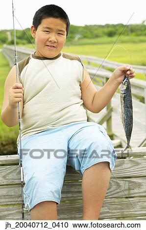 Young boy sitting holding a fishing rod and a fish View Large Photo Image Stock Image - Young boy sitting holding a fishing rod and a fish. Fotosearch