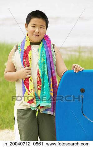 Stock Image - Young boy standing holding a boogie board. Fotosearch