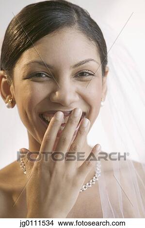 Picture - Young bride smiling with her hand on her mouth looking at camera. Fotosearch
