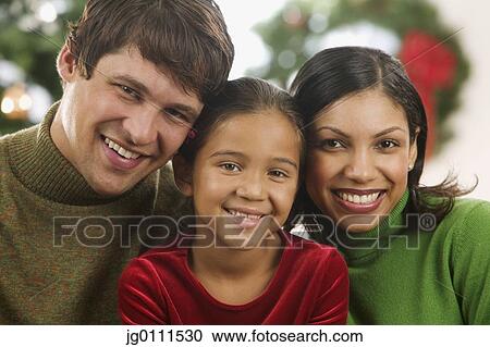 Young couple and their child looking at camera smiling with a Christmas tree in the background View Large Photo Image Stock Image - Young couple and their child looking at camera smiling with a Christmas tree in the background. Fotosearch