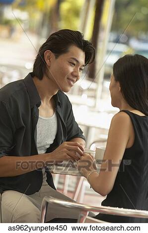 Stock Image - Young couple sitting together at a table in an outdoor cafe. Fotosearch