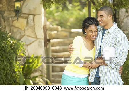 Young couple standing together holding each other View Large Photo Image Stock Photo - Young couple standing together holding each other. Fotosearch