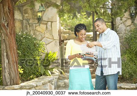Young couple standing together reading a sheet of paper View Large Photo Image Stock Photo - Young couple standing together reading a sheet of paper. Fotosearch