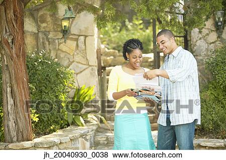 Young couple standing together reading a sheet of paper View Large Photo Image Stock Photo - Young couple standing together reading a sheet of paper. Fotosearch