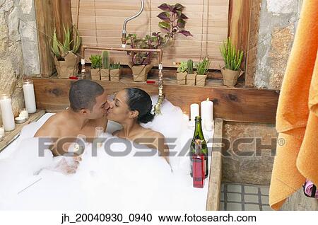 Stock Image - Young couple together in a bubble bath kissing. Fotosearch