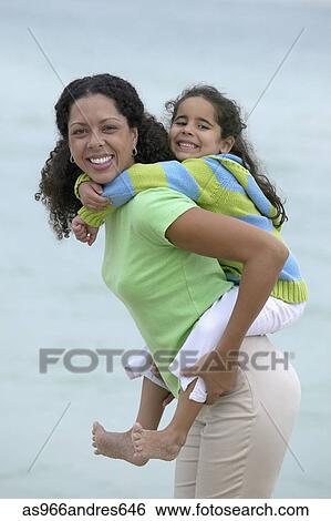Stock Photograph - Young girl piggyback riding on a young woman at the beach. Fotosearch