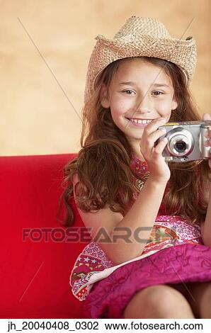 Stock Image - Young girl sitting on a couch holding a camera. Fotosearch