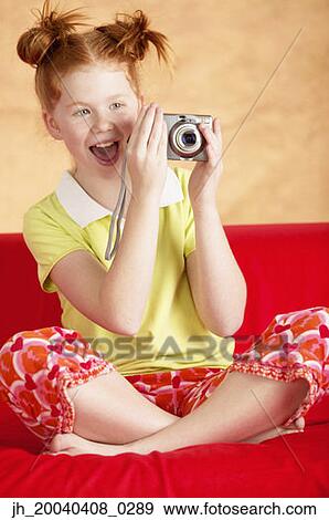Young girl sitting on a couch holding a camera View Large Photo Image Stock Photo - Young girl sitting on a couch holding a camera. Fotosearch