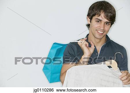 Stock Photograph - Young man holding a shirt on a coat hanger and a shopping bag. Fotosearch