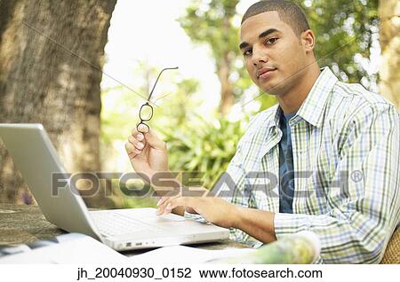 Young man sitting at a table working on a laptop View Large Photo Image Stock Image - Young man sitting at a table working on a laptop. Fotosearch