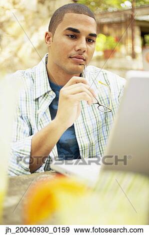 Young man sitting at a table working on a laptop View Large Photo Image Stock Photo - Young man sitting at a table working on a laptop. Fotosearch