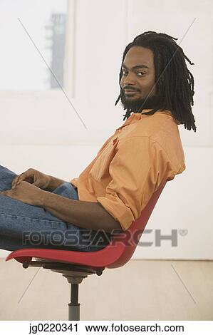 Young man sitting on a chair looking at camera View Large Photo Image Stock Image - Young man sitting on a chair looking at camera. Fotosearch