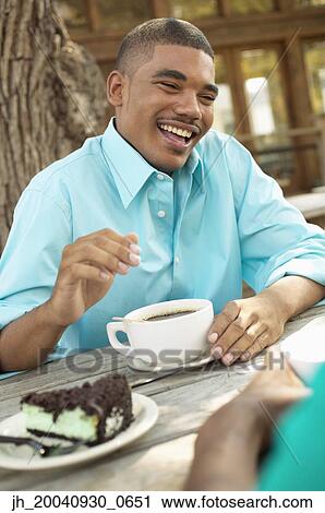 Young man sitting outdoors at a table holding a cup of coffee View Large Photo Image Stock Image - Young man sitting outdoors at a table holding a cup of coffee. Fotosearch