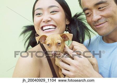 Young woman and a mid adult man standing together holding a puppy dog View Large Photo Image Picture - Young woman and a mid adult man standing together holding a puppy dog. Fotosearch