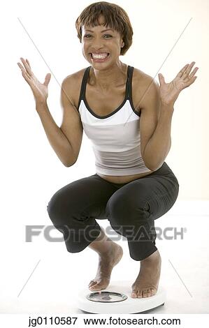 Stock Photo - Young woman crouching on a weighing scale. Fotosearch