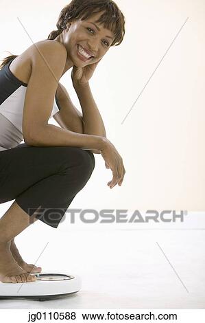 Young woman crouching on a weighing scale View Large Photo Image Stock Photo - Young woman crouching on a weighing scale. Fotosearch