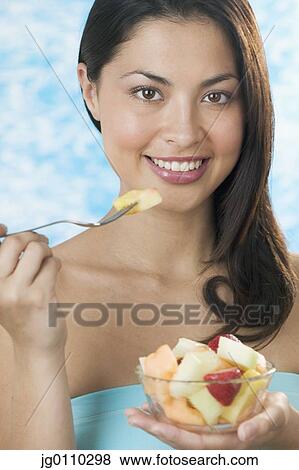 Young woman eating a bowl of fruit View Large Photo Image Stock Photo - Young woman eating a bowl of fruit. Fotosearch