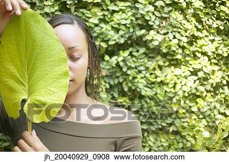 Stock Photo - Young woman holding a leaf in front of her face. Fotosearch