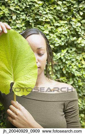 Stock Photo - Young woman holding a leaf in front of her face. Fotosearch
