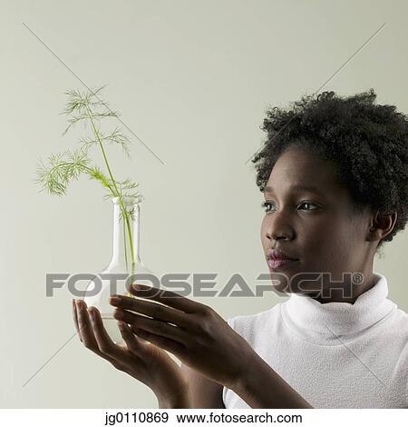 Stock Photo - Young woman holding a plant growing in a glass flask. Fotosearch