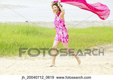 Stock Photo - Young woman holding a sarong over her head running. Fotosearch